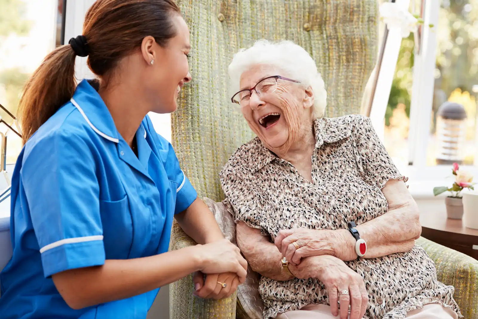 Smiling carer holding hands with an elderly woman in a sunny room